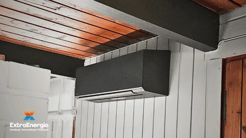 Musta ilmalämpöpumpun sisäyksikkö mökin puuseinällä.